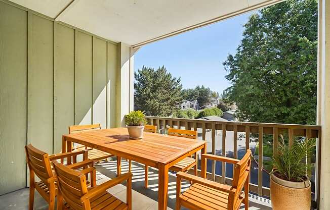 A wooden table and chairs on a balcony with a potted plant.