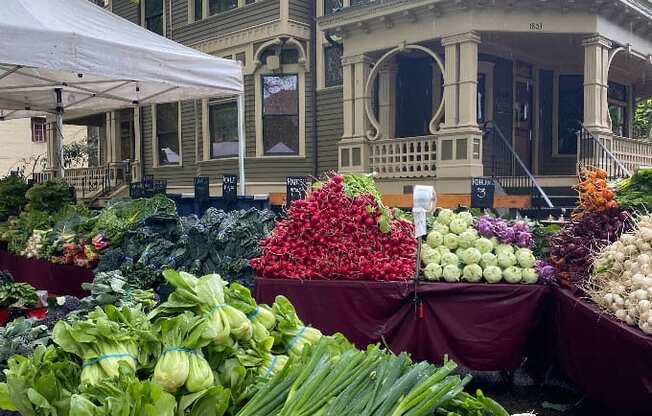 A market with vegetables on display in front of a Victorian style house.