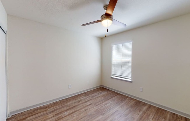 the spacious living room with wood flooring and a ceiling fan