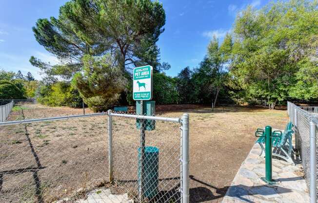 Community gated dog park with pet waste station at entrance and bench inside the fenced area. 