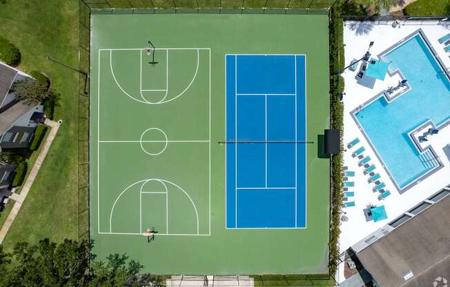 A tennis court is surrounded by a pool and a house.