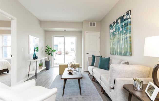 A living room with a white sofa, a white chair, a wooden coffee table, and a painting on the wall.