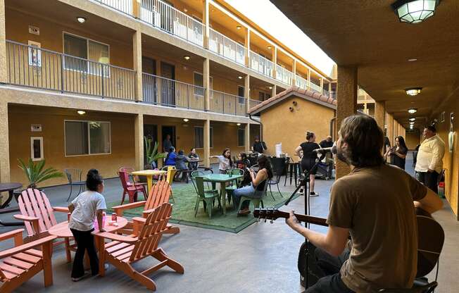 a man playing a guitar in a courtyard with people sitting at tables