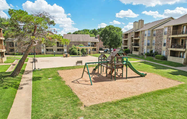A playground with a green slide and a brown sandbox in the middle of a grassy area.