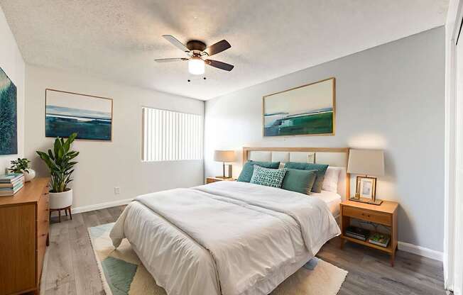 A bedroom with a large bed, a ceiling fan, and two pictures on the wall.