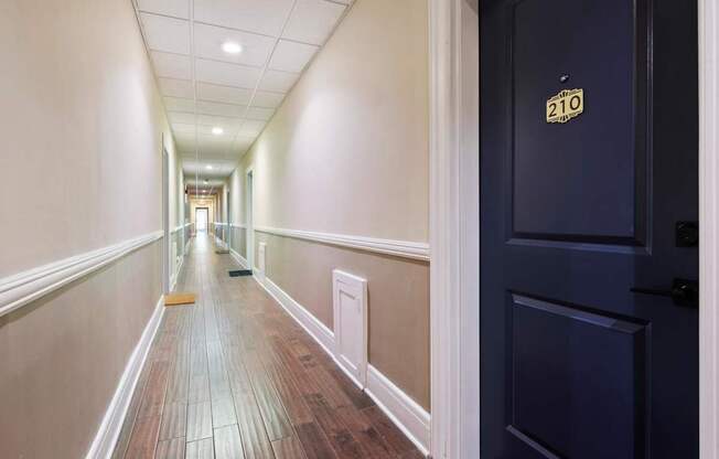 A hallway with a door on the right and a number 210 on the door.