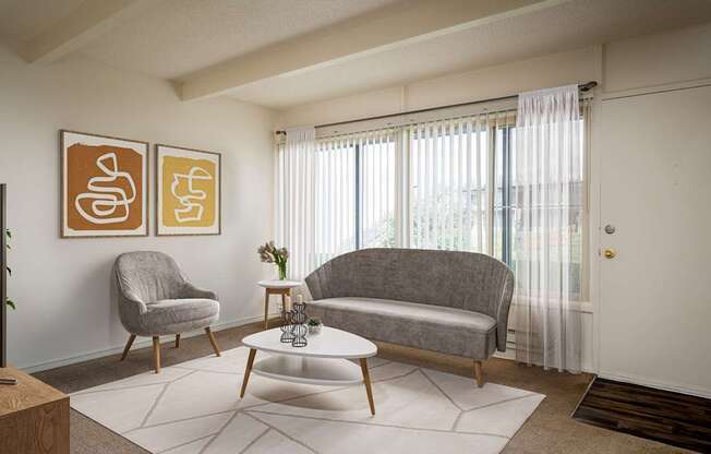 A living room with a grey couch, a grey armchair, a white coffee table, and two framed artworks on the wall.
