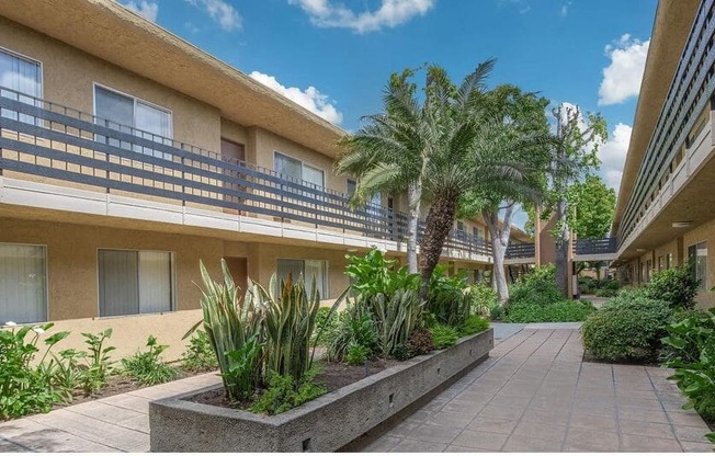 a building with palm trees in a courtyard at Villa La Paz Apartments, Bellflower, California