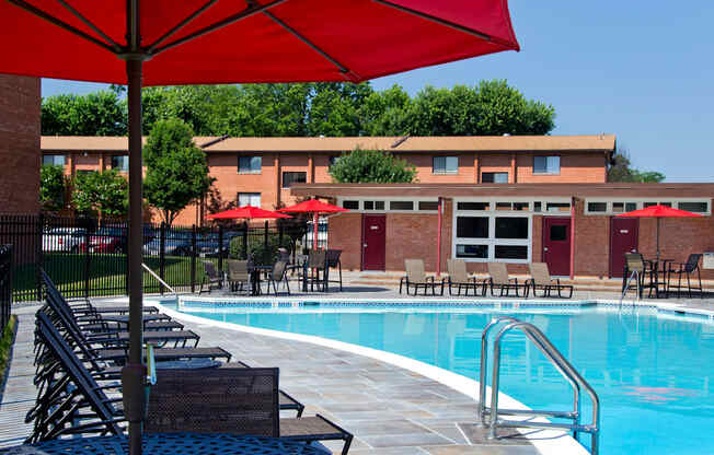 A pool area with chairs and umbrellas in front of a building.
