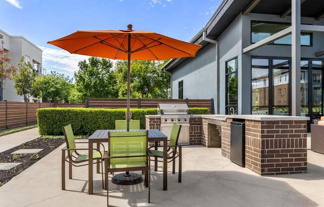 A patio with a table and chairs under an orange umbrella.