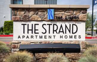 A sign for The Strand Apartment Homes is displayed in front of a building.