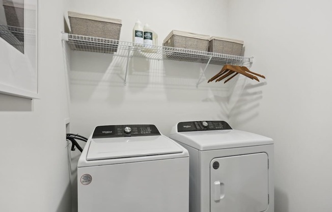 A laundry room with a washer and dryer and a shelf with baskets and a handbag.