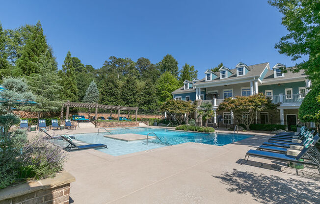 a swimming pool with chairs and a house in the background