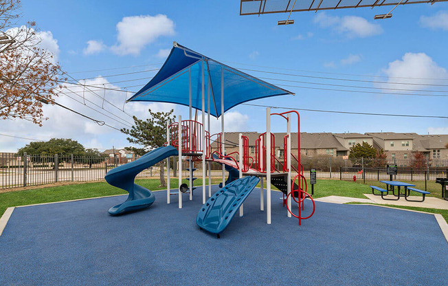 Community Playground with Slide and Blue Canopy at Bridges at Oakbend Apartments in Lewisville, TX.