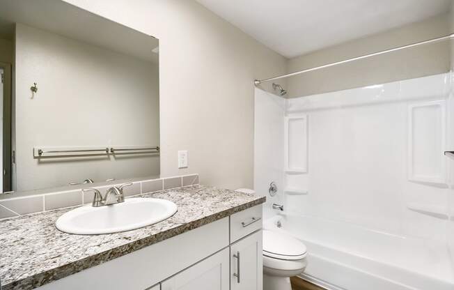 A full bathroom with a vanity sink, under-sink cabinet storage, a toilet, shower, and bathtub. Staged with a shower curtain, hand soap, and towels.at Wildflower, Kennewick, WA