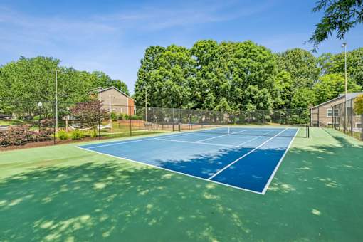 A tennis court surrounded by trees and a fence.