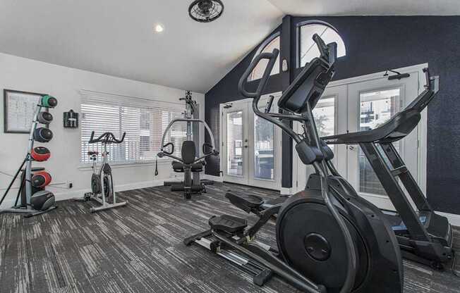 A black treadmill and a black stationary bike are in a room with a window.