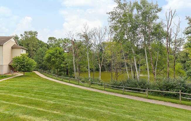 A house is on the left of a grassy area with a fence and trees.