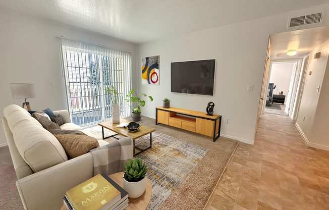 Bridgeside Landing Apartments in Taylorsville, Utah, Living area with tan couch, flatscreen television on wall, balcony off the room, hallway back to bedroom.