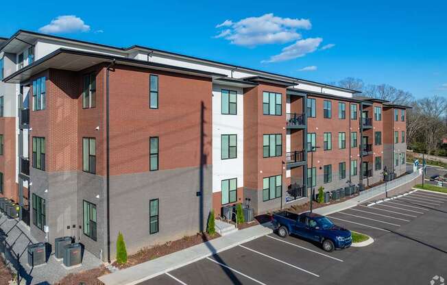 A blue truck is parked in a parking lot in front of a red and grey building.