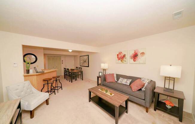 A living room with a couch, a chair, a coffee table, and a dining table at Emerald Park Apartments in Kalamazoo, MI
