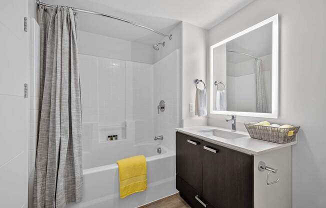 A bathroom with a white tub, sink, and a grey shower curtain.