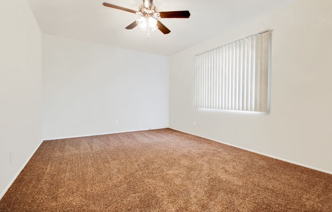 Bedroom with carpeted floors, ceiling fan and vertical window blinds on the right