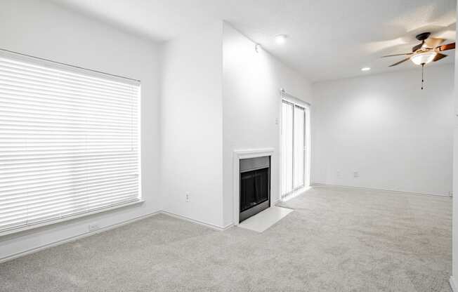 an empty living room with a fireplace and a ceiling fan