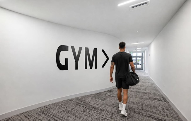 A man walking in a hallway with a Gym sign on the wall.