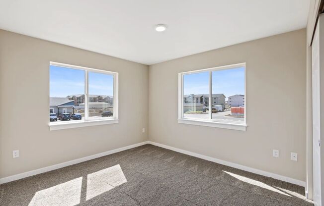 an empty bedroom with two windows and a carpeted floor