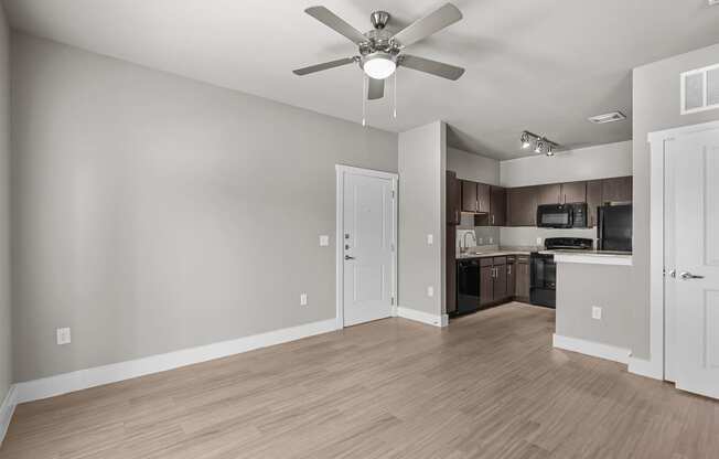an empty living room with a ceiling fan and a kitchen