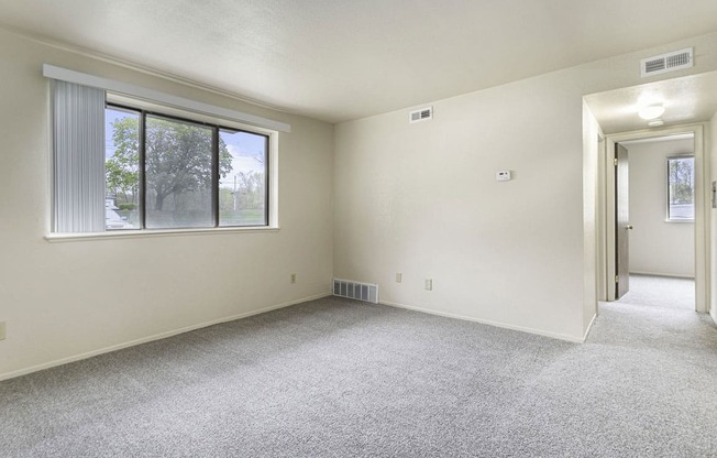 an empty living room with a large window and carpeting