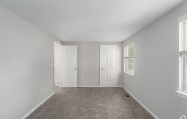 an empty bedroom with two doors and a carpeted floor