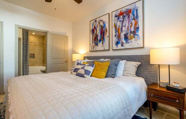 A bedroom with a large bed and two abstract paintings on the wall.