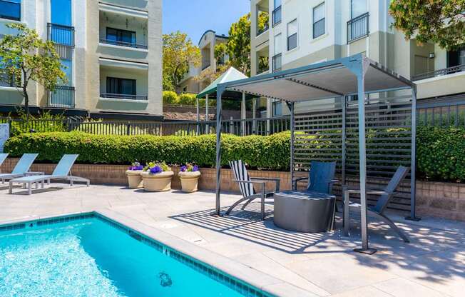 A pool with a hot tub and chairs under a canopy.