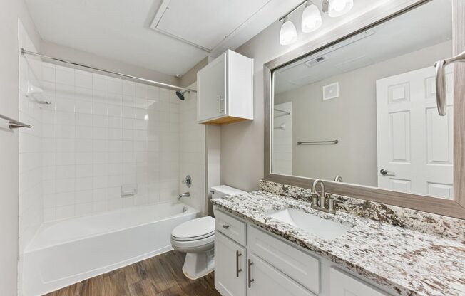A white bathroom with a marble countertop and a white bathtub.