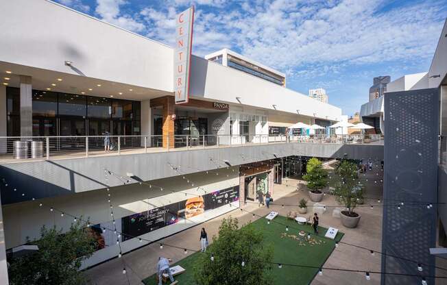 A view of a shopping mall with a green lawn and people walking around.