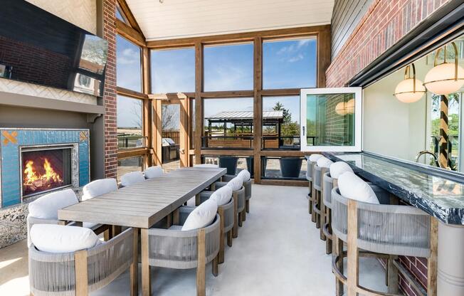 Screened-in porch with a harvest dining table, an adjacent catering kitchen and entertainment lounge inside, plus a cozy outdoor fireplace.
