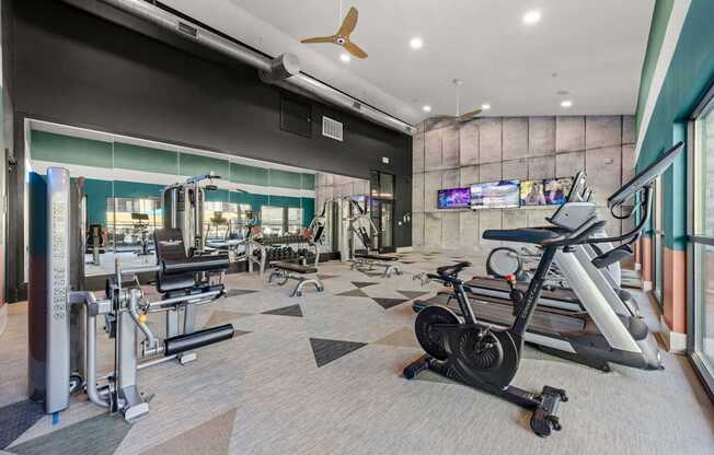A gym with a variety of equipment including treadmills, weights, and a television. at Bridge at Tech Crossing, Austin, 78753