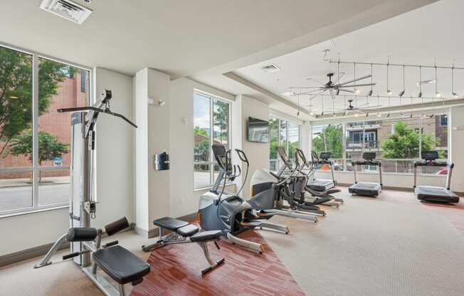 a gym with a row of exercise machines and windows