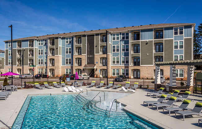 a swimming pool with lounge chairs in front of an apartment building