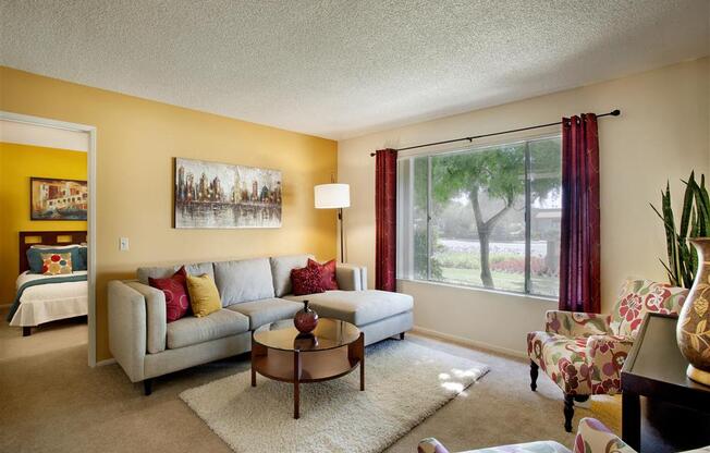 Goleta, CA Apartments- Patterson Place- Yellow Accent Wall, Large Window, Wall-to-Wall Carpet, and Circle Coffee Table