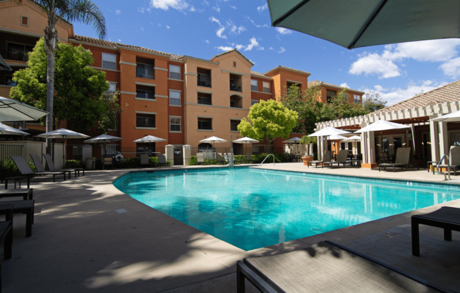 A large swimming pool surrounded by a patio with chairs and umbrellas.