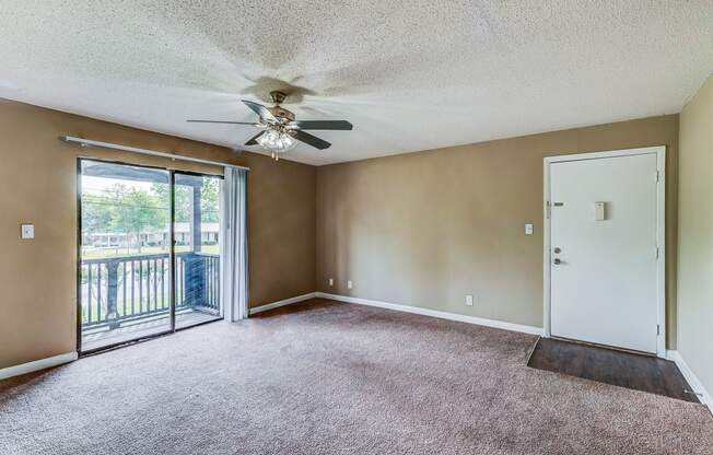 an empty living room with a ceiling fan and a door to a balcony