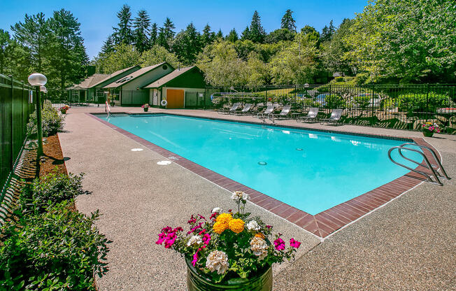 A pool surrounded by trees and a fence with a flower pot in the foreground.