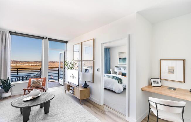 Bright, open living with a dedicated workspace and balcony views just beyond.