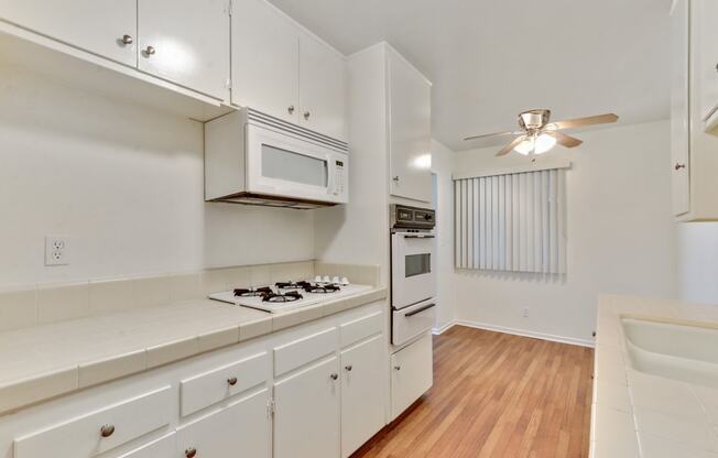 Kitchen with white gas cooktop over microwave, White Oven, Wood Style floors throughout dining area with ceiling fan