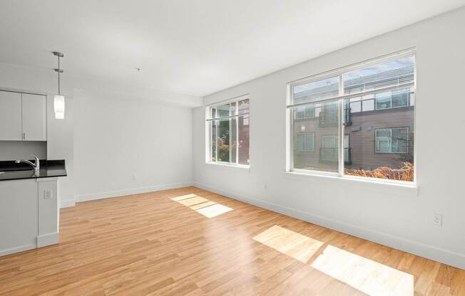 A room with wooden floors and a kitchen area with white cabinets.
