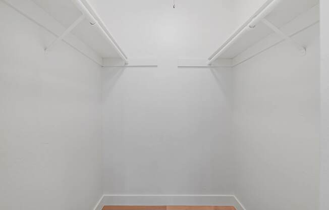 A white room with a wooden floor and two white shelves on the wall.