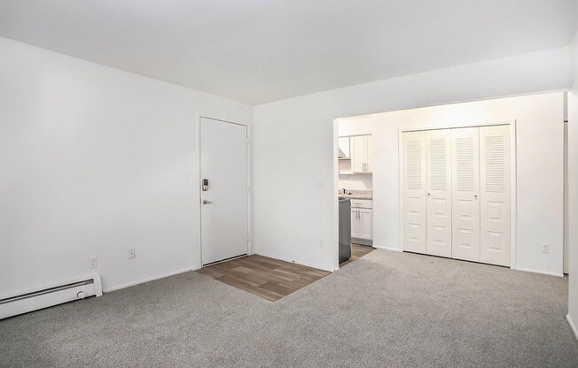 an empty living room with a kitchen in the background